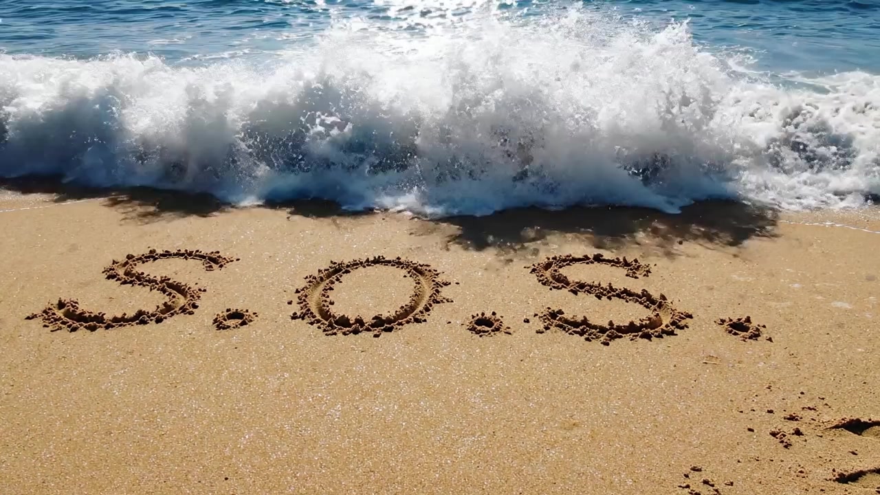 Et nødsignal lavet af sand: SOS-beskeden fanget på en strand med blide bølger og glimtende vand, der reflekterer sollyset.