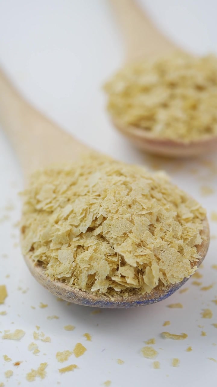 Fiocchi di lievito alimentare in cucchiai di legno su sfondo bianco
