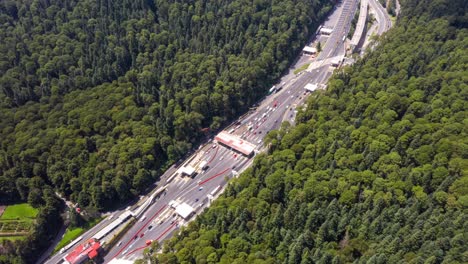 Hiperlapso:-Vuelo-Giratorio-Sobre-La-Cabina-De-Peaje-De-La-Autopista-Con-Tráfico-Que-Viaja-En-La-Autopista-Y-Misteriosas-Sombras-Místicas-De-Nubes-Oscuras-Fluyen-Más-Allá-Del-Paisaje-Escénico-Del-Bosque-De-árboles-Verdes,-Ciudad-De-México,-Drone-Circular