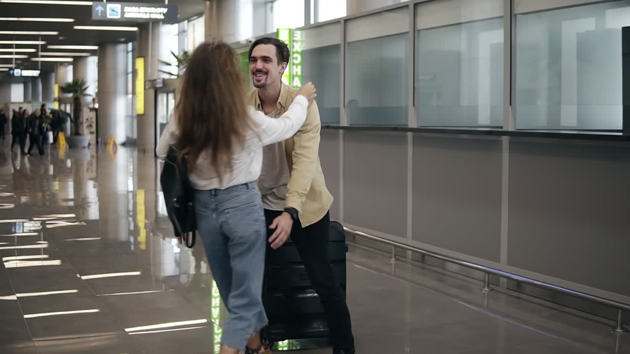 Bearded young man with suitcase, waiting for his girlfriend, in airport flying back home from business trip after long