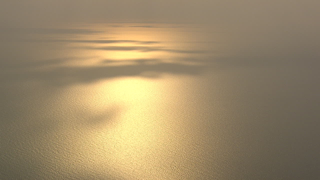 setting sun reflects on the sea with some patches of shadow casted by the clouds