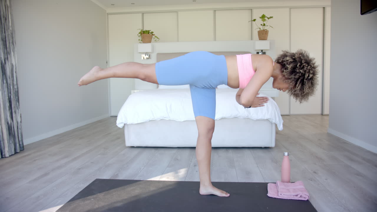 Practicing yoga, woman balancing on one leg on yoga mat in bedroom