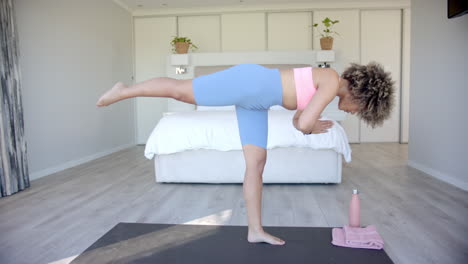 practicing yoga, woman balancing on one leg on yoga mat in bedroom