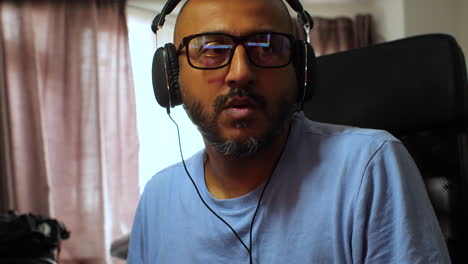 South-Asian-man-wearing-glasses-and-headphones-listening-to-music-at-home-bopping-head