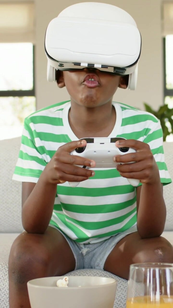 Vertical video: Reacting to VR headset child in striped shirt pressing controller voicing at home
