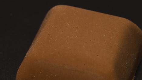 piece of chocolate macro shot, detail close up in 4k, small square of milk chocolate rotating over black surface background