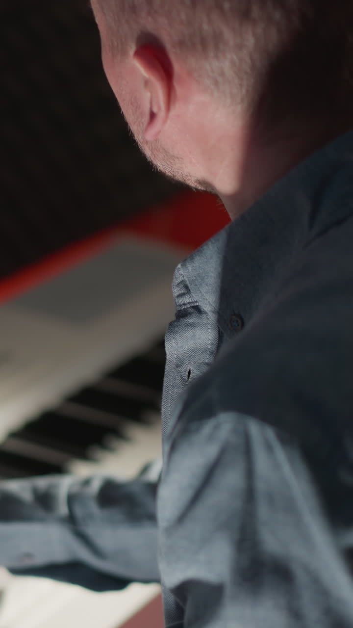 disparo lateral de un hombre con una camisa de manga larga de color claro tocando un piano blanco. ambientado contra un fondo oscuro e a prueba de sonido, centrándose en la intensidad y la concentración del músico mientras actúa