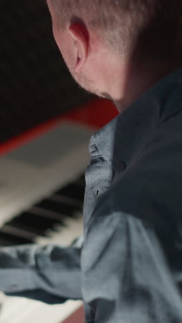 disparo lateral de un hombre con una camisa de manga larga de color claro tocando un piano blanco. ambientado contra un fondo oscuro e a prueba de sonido, centrándose en la intensidad y la concentración del músico mientras actúa