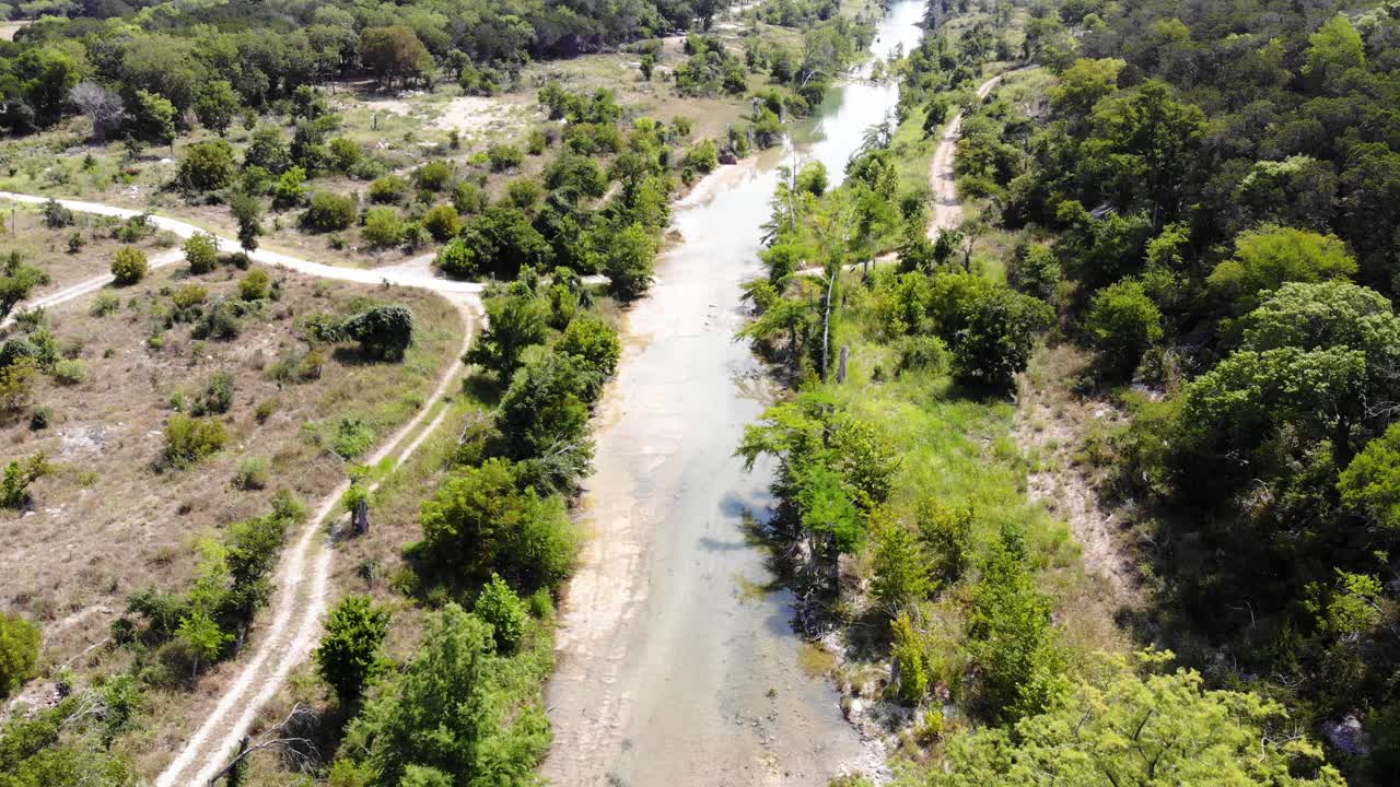 Luftoptagelse af Blanco-floden i Wimberly, TX. En vej løber højt over floden, parallelt med den, og krydser den derefter til den anden side.