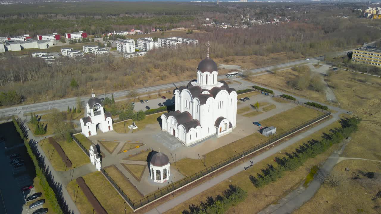 Aerial left to right panning footage og a large white russian style church called Icon of the mother in Lasnamäe Estonia during a spring sunny day with asphalt roads around the holy building.
