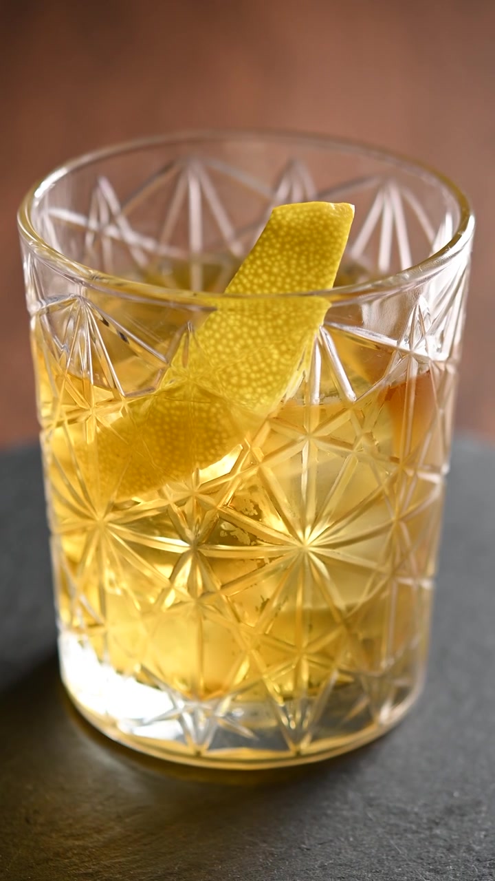 Cocktail Rusty Nail in rotazione in un bicchiere old fashioned con ghiaccio, primo piano di una bevanda ambrata.