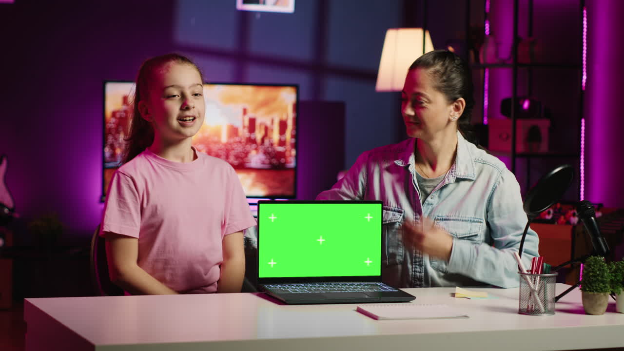 Figlia e madre in home studio filmano insieme accanto al portatile a schermo verde