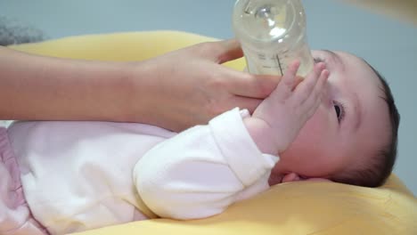 노란색 쿠션에 누워있는 동안 어머니가 젖병에 영양을 공급하는 한국 아기