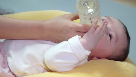 korean baby being bottle fed nutritions by mother while lying on yellow cushion