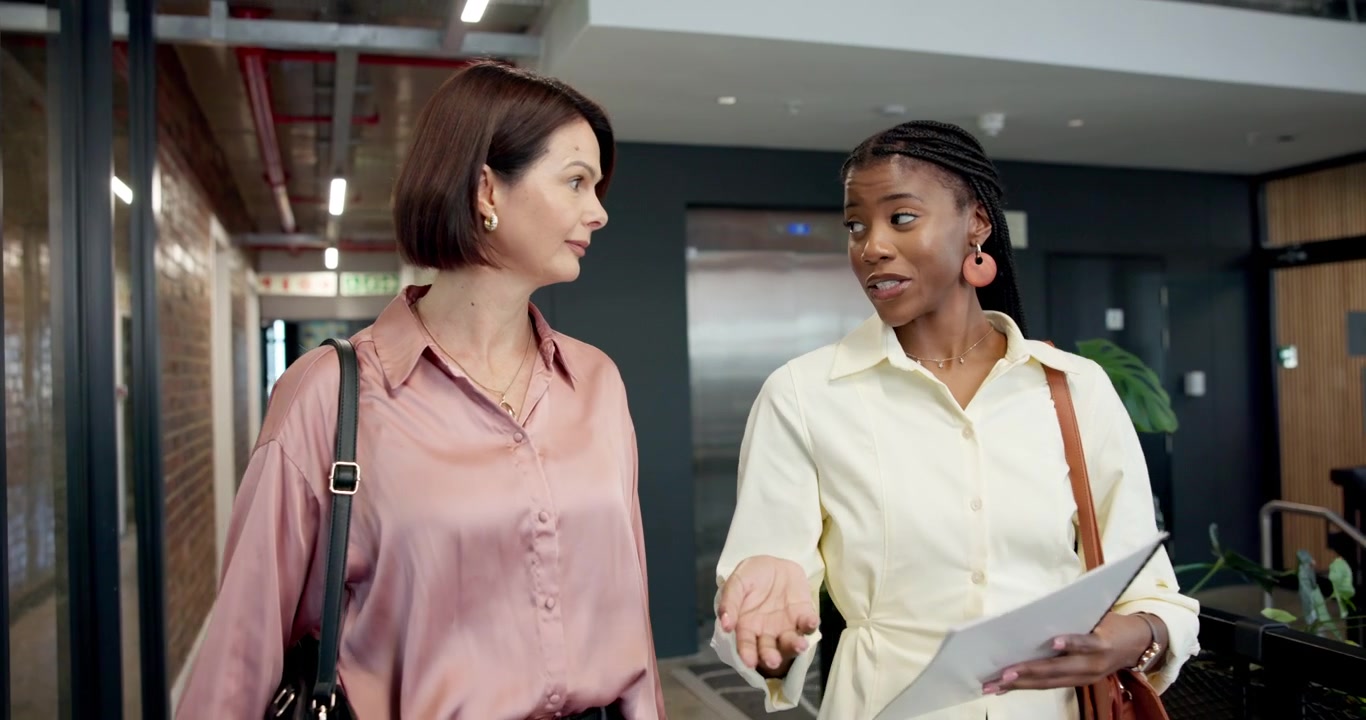 Two Professional Women Discussing Documents While Walking Through Modern Office