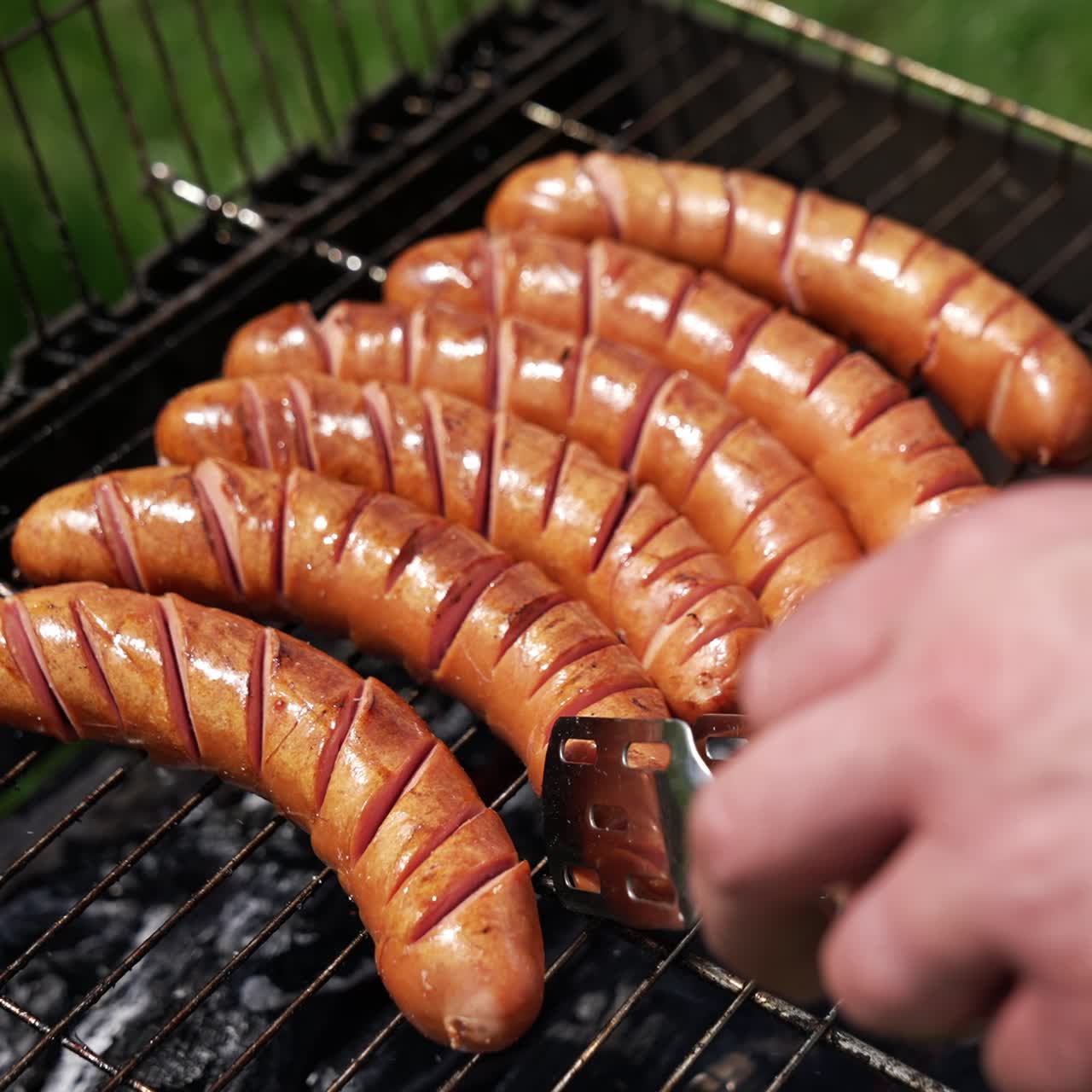 Cooking sausages in smoke outdoors. Tasty roast food on charcoal for picnic. Chef cooking grilled beef hot dog sausage on grill. Close-up