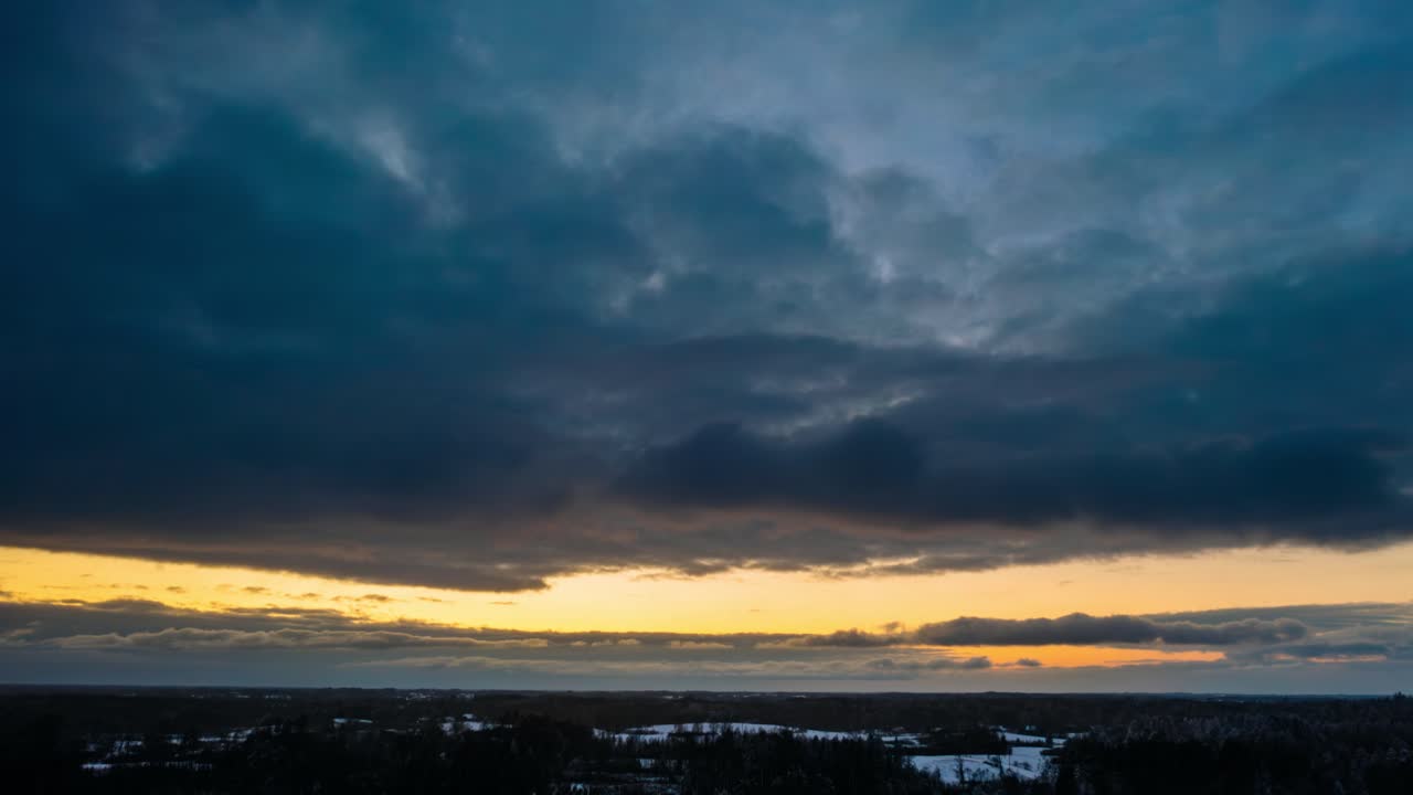 Aerial sunset hyperlapse with snow clouds rolling in. Winter snowy weather in countryside. Drone timelapse of snow falling.