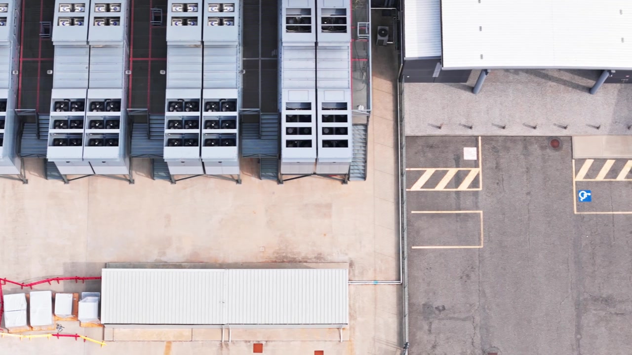 Aerial top-down view of a large-scale data center. Numerous powerful hvac cooling units operating on the rooftop of the building