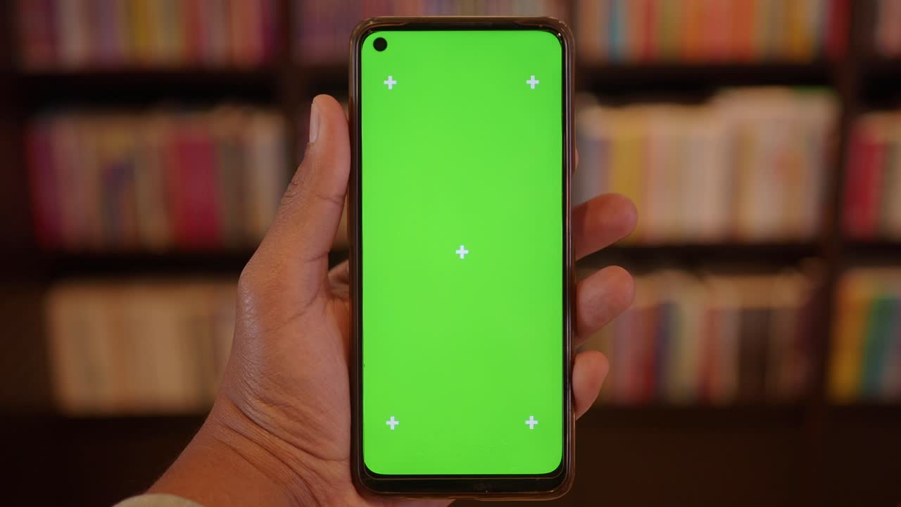 Mano che tiene uno smartphone con schermo verde in una biblioteca
