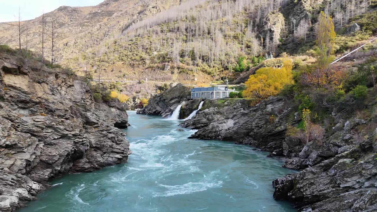 Drone footage captures the Kawarau River and hydroelectric power station amidst autumn foliage in Central Otago, New Zealand