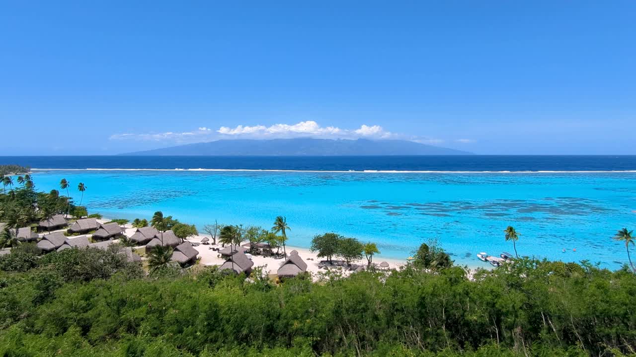 Scenic panoramic view from lookout on Moorea Island in French Polynesia with views of Tahiti Island, crystal clear blue ocean water and beach hut accommodation on white sand beach