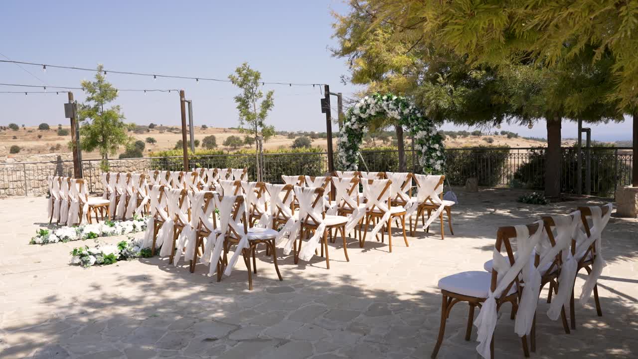 A lovely outdoor wedding setup features rows of chairs facing a decorative altar. With a stunning view and sunny weather, this setting is perfect for a memorable celebration