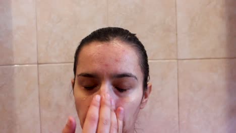 young woman using skin care product to clean her face, close up