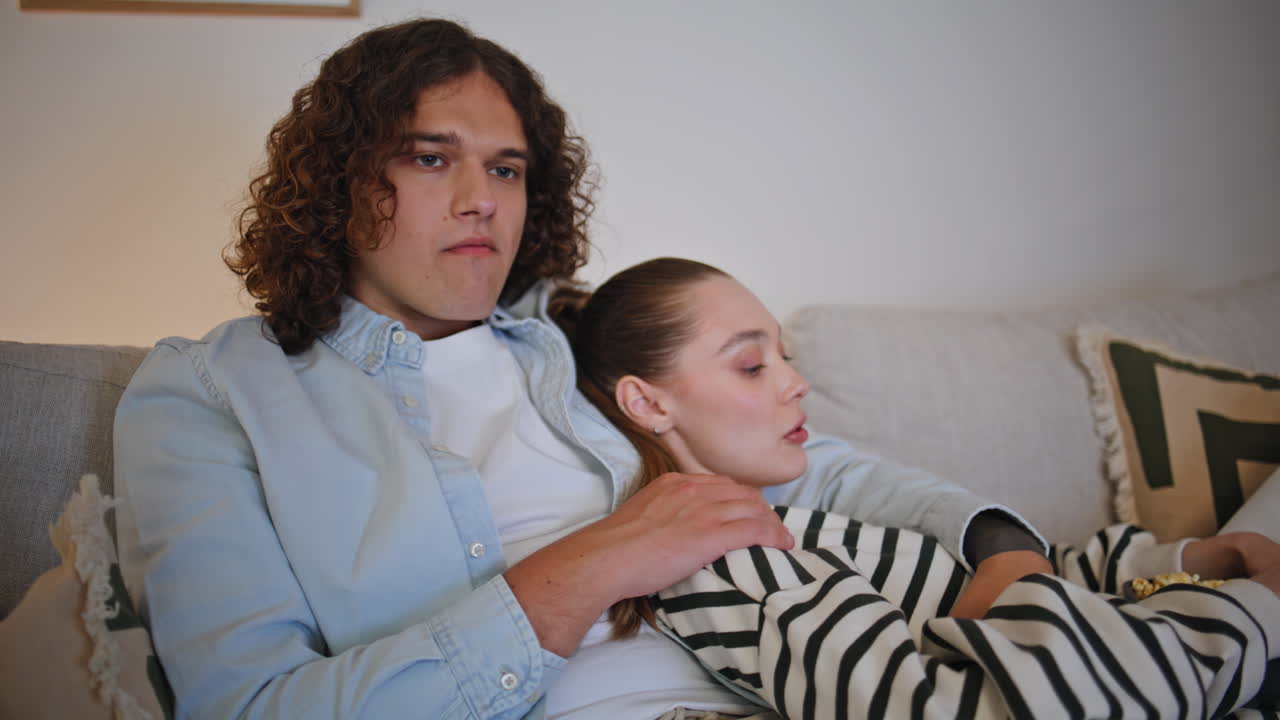 Primo piano di una coppia che si gode un film in TV mangiando popcorn sul divano di casa la sera