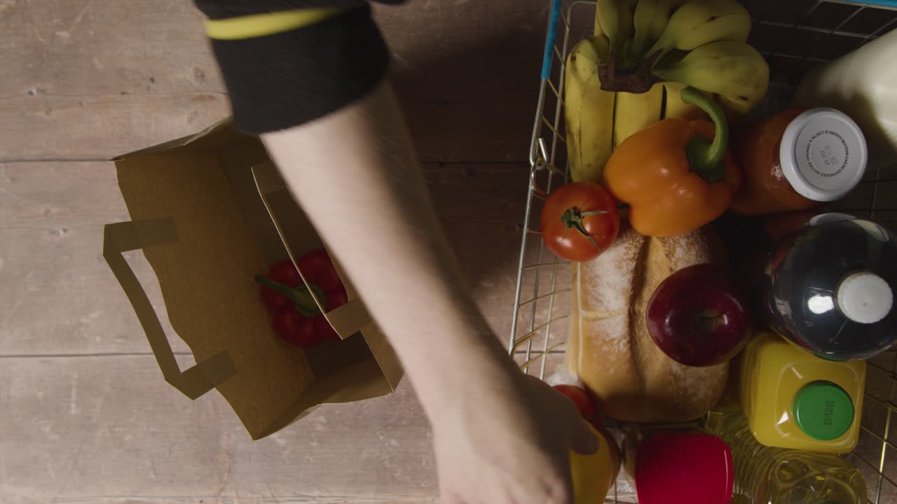fotografía cenital de una persona empacando alimentos frescos básicos de la cesta de la compra de alambre del supermercado en una bolsa de papel