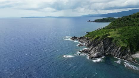 Luftaufnahme-Der-Klippe-Einer-Tropischen-Insel-Mit-Türkisfarbenen-Meereswellen,-Die-Gegen-Zerklüftete-Felsen-Und-üppiges-Grün-Krachen