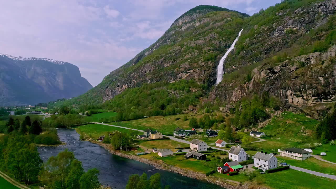 drone aéreo hacia adelante toma de cascada a lo largo de la ladera de la montaña en el río gronsdalslona en noruega con casas de pueblo en las estribaciones durante el día
