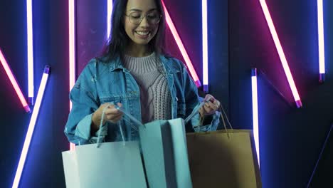 young girl in blue denim jacket with shopping bags on neon lamps background.