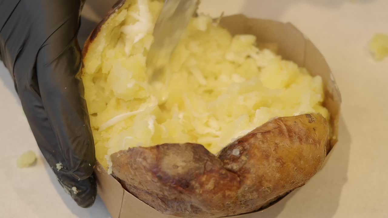 Primo piano di una mano che schiaccia una patata al forno con un coltello
