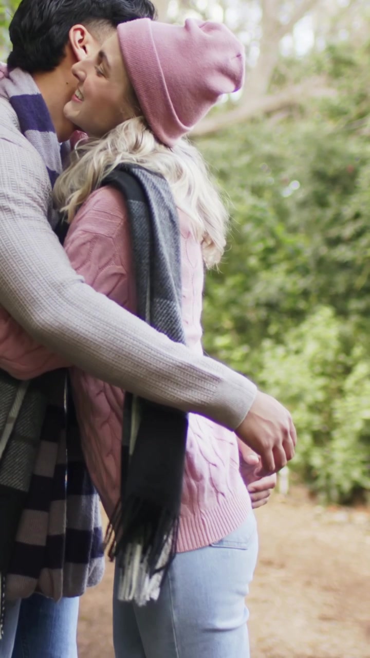 Video verticale: Vedendo il partner, donna con berretto rosa che si china per un bacio sulla guancia su un sentiero nel bosco, abbracciandosi.