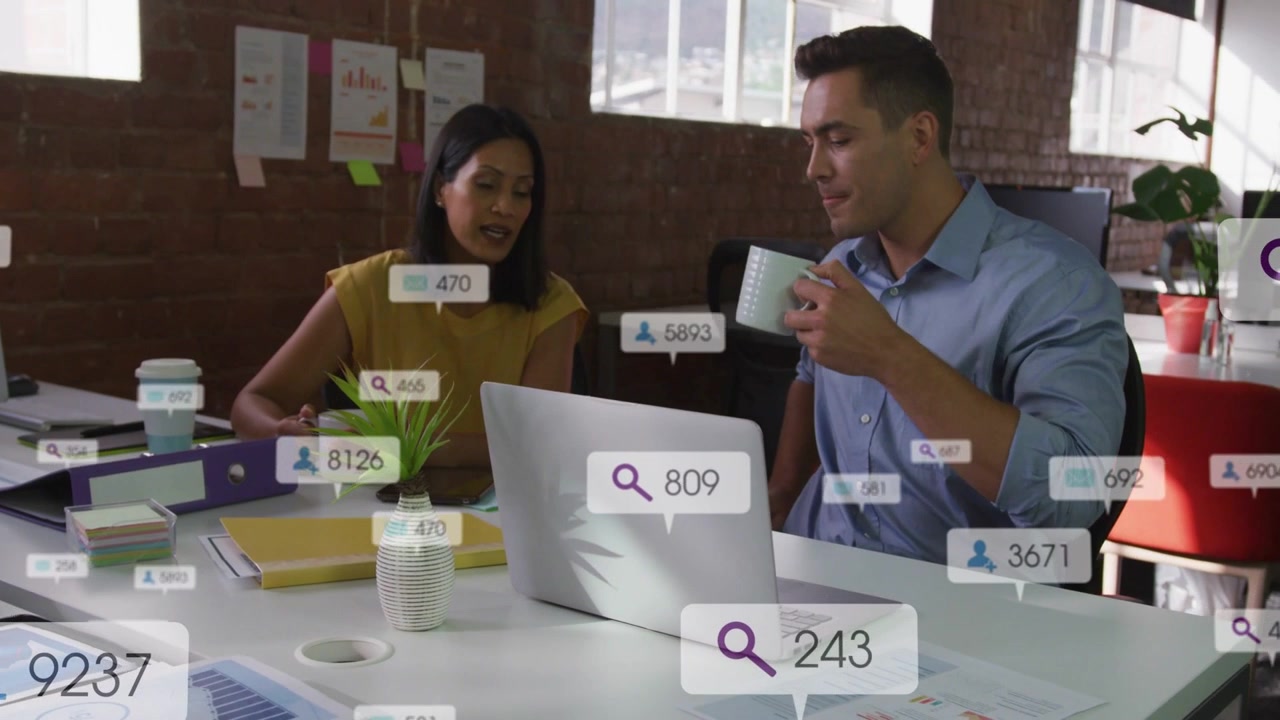 Diverse coworkers at desk reacting to UI badges, reviewing laptop, pointing at papers, holding mugs