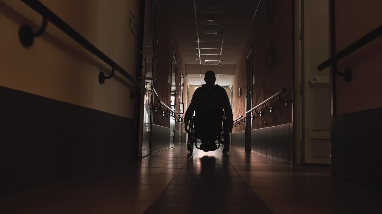 Uomo con disabilità in sedia a rotelle che percorre un lungo corridoio.