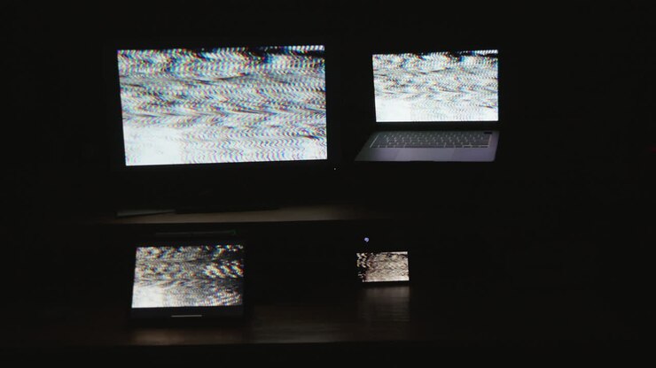 Four digital computer device screens flashing a strobing static noise pattern in a dark room