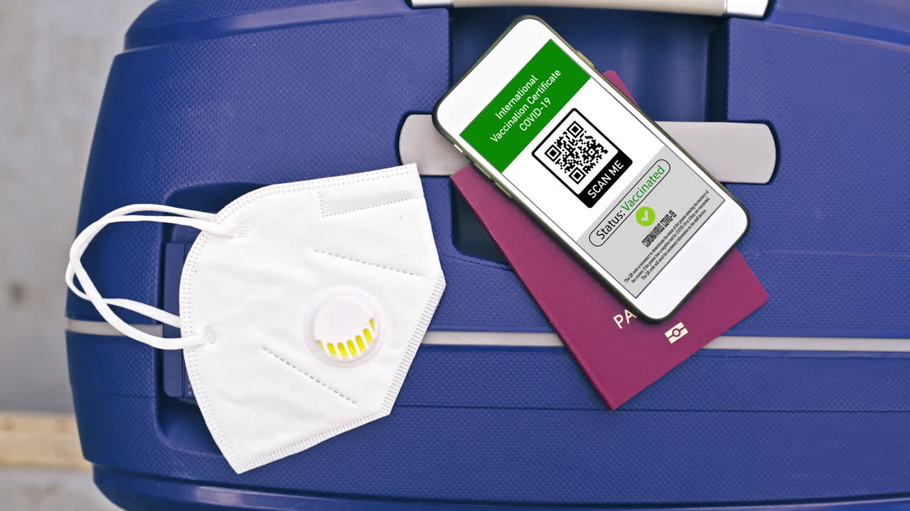 Passport and smartphone with International Vaccination Certificate COVID-19 QR code on suitcase with mask