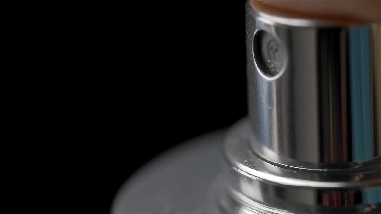 Closeup of silver spray bottle pushed down to emit mist of liquid against black background