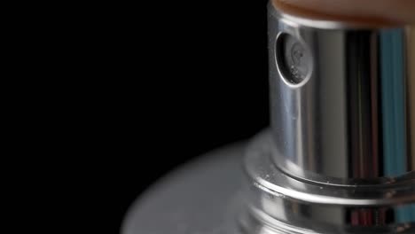 closeup of silver spray bottle pushed down to emit mist of liquid against black background