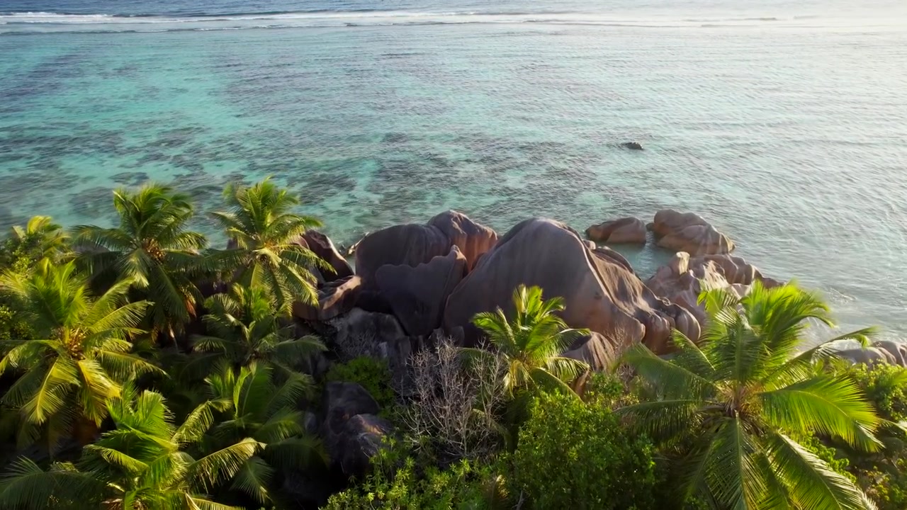 Garis pantai La Digue bersinar dengan pohon palem dan granit di tepi laut. Pemandangan udara