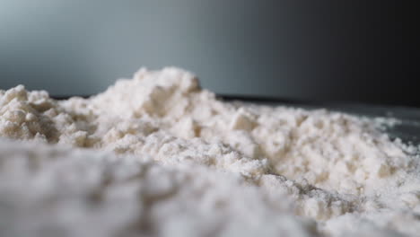 unsifted flour lies spilled on table against dark grey wall