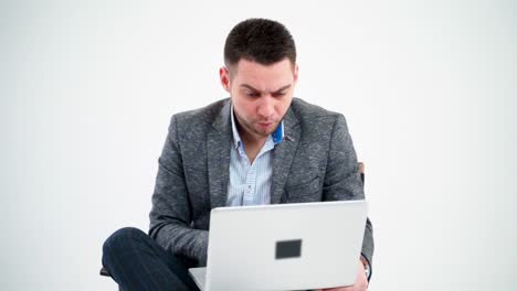 grieved businessman looking into the laptop. pensive male freelancer working on a modern gadget while sitting alone on white background.