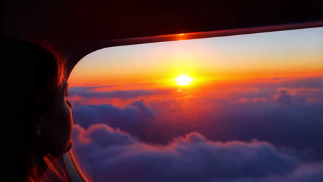 passenger looks out airplane window at a beautiful sunset over the clouds