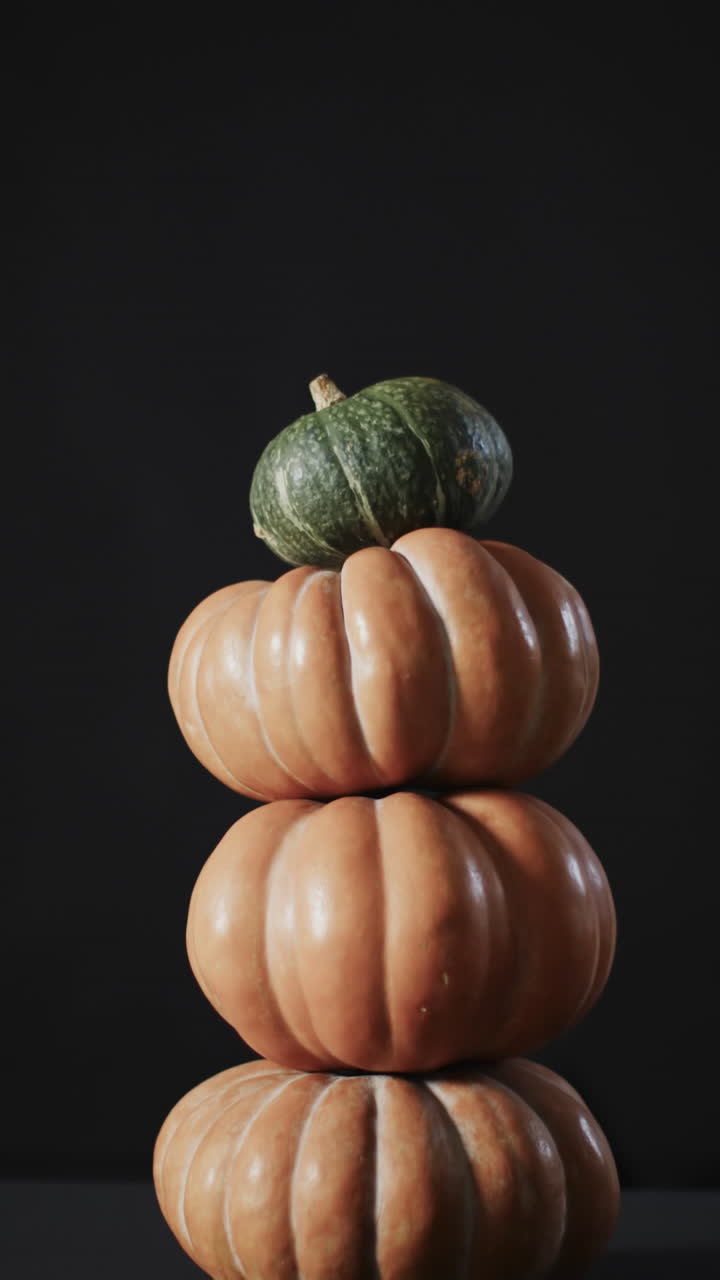 Vertical video of stack of pumpkins on black background