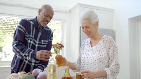 Happy-senior-biracial-couple-unpacking-shopping-bags-in-kitchen,-slow-motion