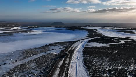 car driving on a snowy winter road through a desolate volcanic landscape