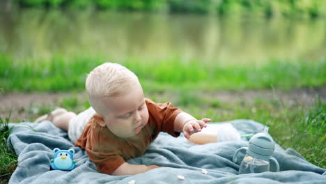 little blond baby boy lying on the blue plaid outdoors. active child picking pop-corn. kid resting in the nature.