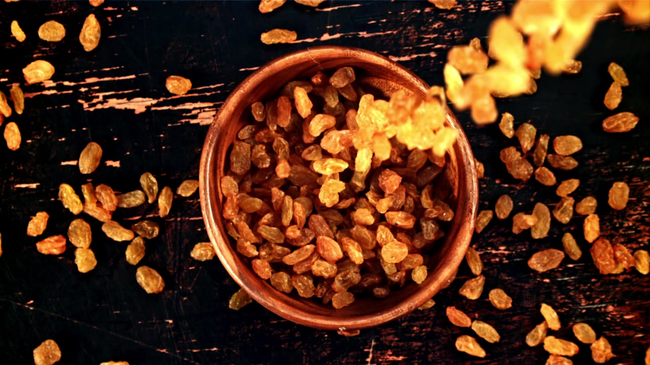 Golden Raisins Falling into a Wooden Bowl in Slow Motion