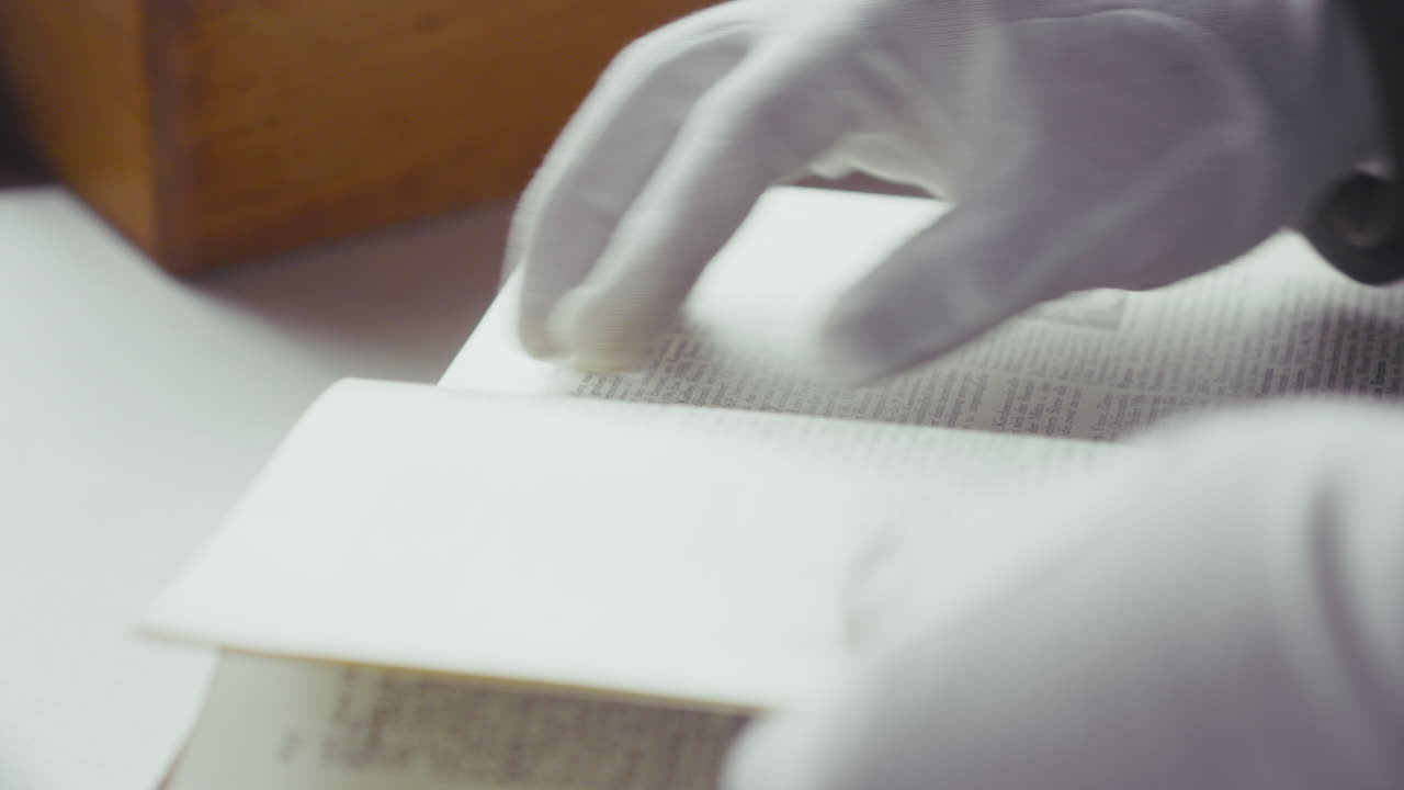 Macro inquadratura di mani guantate di bianco che sfogliano le pagine di un vecchio libro illustrato, evocando ricerca archivistica, scoperta e conservazione della conoscenza.
